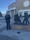 Teen stands beside a bronze statue of children outside the New Mexico Capitol building.