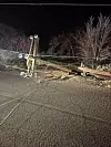 Downed wooden power pole and wires lying across a rural road at night