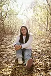 Teen sitting on a leafy woodland path with sun shining through trees