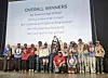 Students onstage with trophies and medals in front of an Overall Winners results screen.