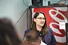 Woman in glasses and blazer speaking in a room with a Coca-Cola cooler behind her.